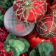 Close-up of Christmas ornaments with red and gold glitter, plaid design, red berries, and eucalyptus leaves.