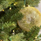Close-up of a shimmering gold Christmas bauble on pine tree branches with warm lights