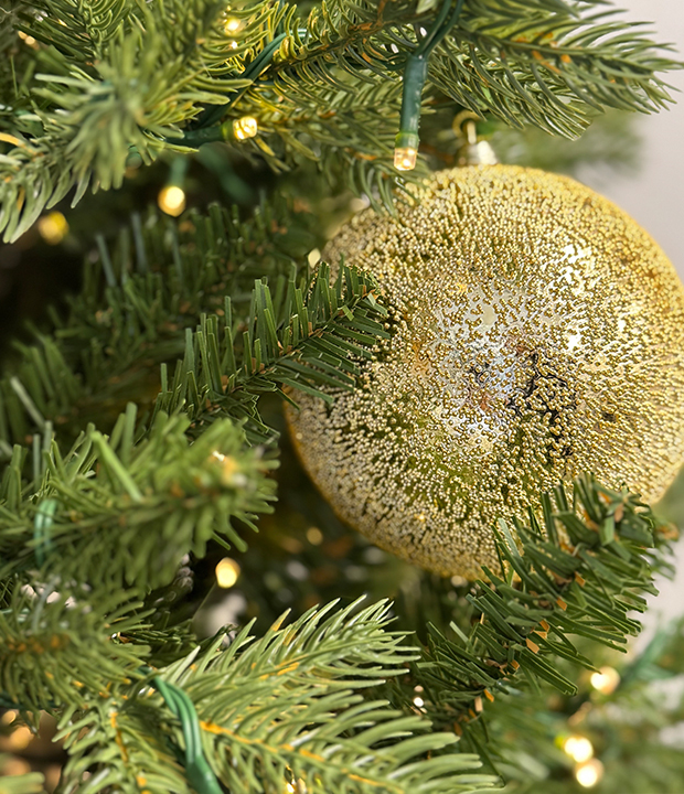 Close-up of a shimmering gold Christmas bauble on pine tree branches with warm lights