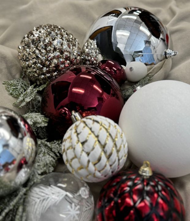 Red, silver, and white Christmas ornaments with glitter and festive patterns on a soft beige background.