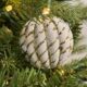 Close-up of a white Christmas ornament with gold zigzag patterns nestled in green pine needles, with warm twinkling lights creating a festive holiday atmosphere.