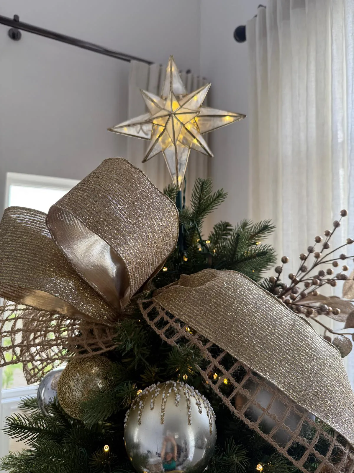 Christmas tree decorated with golden ribbons, shimmering ornaments, and a glowing star topper in a bright festive room