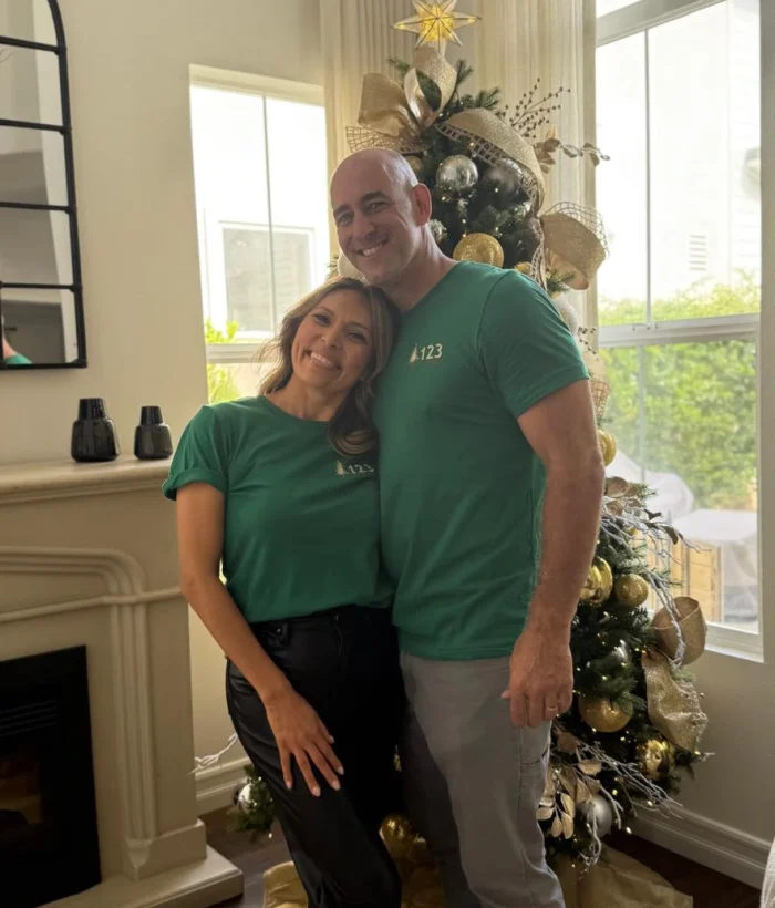 A festive holiday photo of a happy couple posing in front of a beautifully decorated Christmas tree, interior photography, warm lighting, detailed textures, vibrant colors, realistic proportions, flux art style